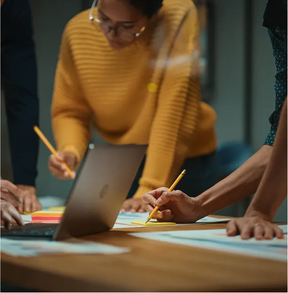 Group works concentrated on a creative concept at the table; focus on teamwork, collection of ideas and project planning with laptop and notes.