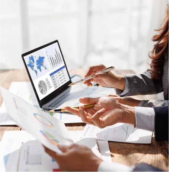 Hands of several people pointing to charts and global statistics on a laptop; focus on data analysis, strategic planning and business intelligence.
