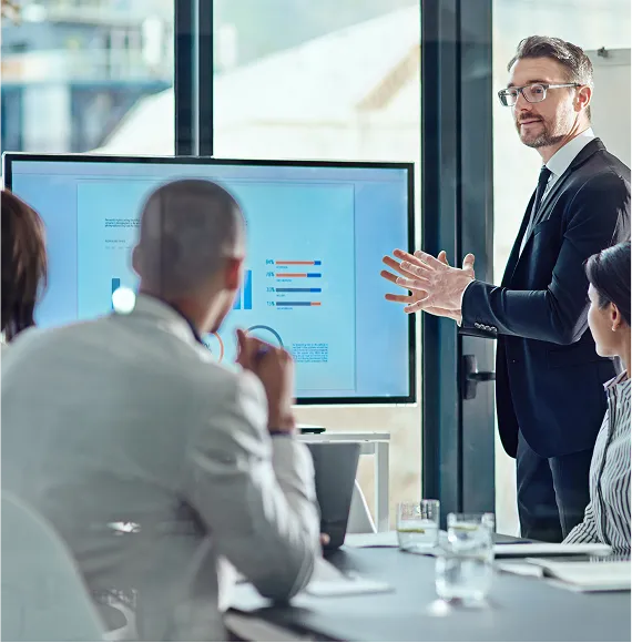 Business presentation in a modern conference room with a business analyst speaking in front of a screen displaying charts, while the team listens attentively.
