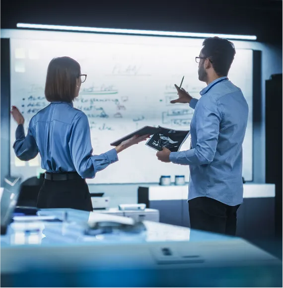 Two people in the high-tech office analyzing concepts in front of a whiteboard; focus on innovation strategy, planning and technical development.