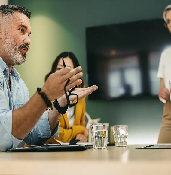 Person gesturing while speaking in a discussion during a meeting; focus on communication, leadership, and decision-making processes in the modern corporate environment.