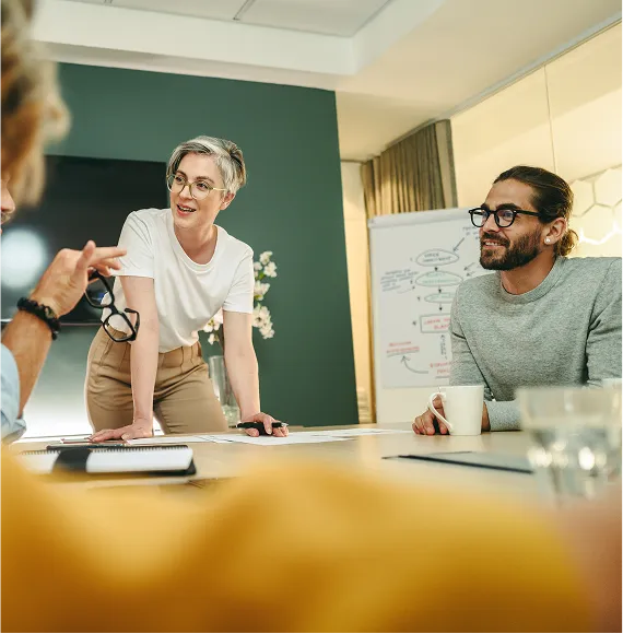 Person stands confidently in a meeting room in front of a team and speaks during a meeting; focus on leadership, team communication and strategic collaboration.